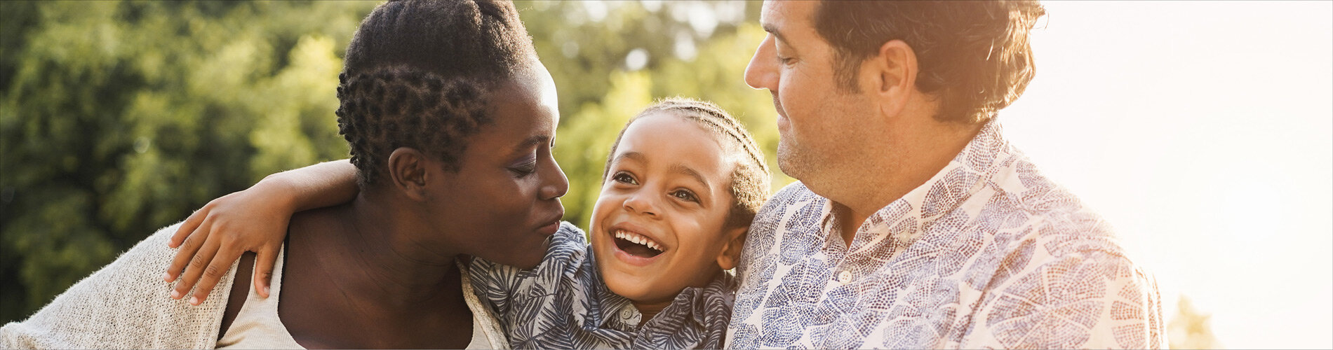 A family standing outside on a sunny day and hugging.