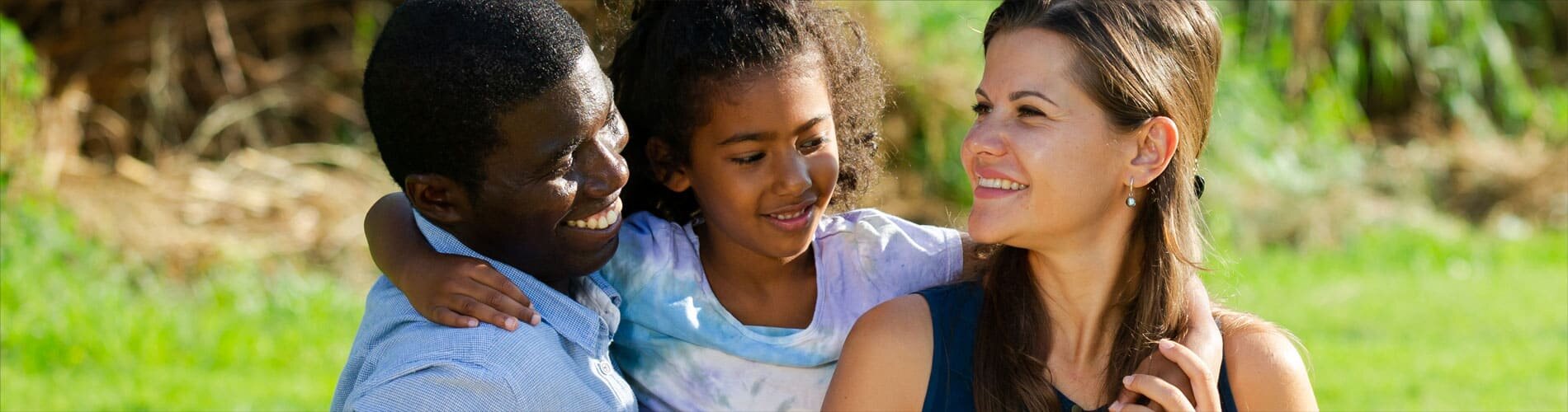 A family standing outside on a sunny day and hugging.